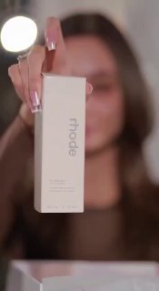 Крупный план коробки и флакона с минималистичной брендинговой упаковкой Rhode, объект держит человек в кадре, фон размытый.