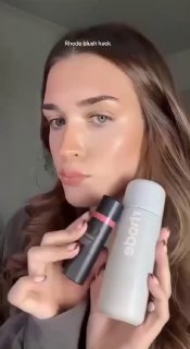 Фотография двух баночек/флаконов косметического бренда Rhode в руках модели, виден глянцевый финиш продукта и рекламный контекст демонстрации.