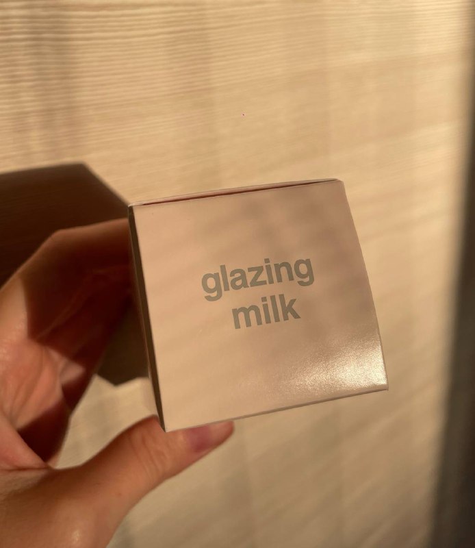 Квадратная коробка с надписью «glazing milk» в руке, мягкое дневное освещение подчёркивает текстуру упаковки и шрифт названия продукта.