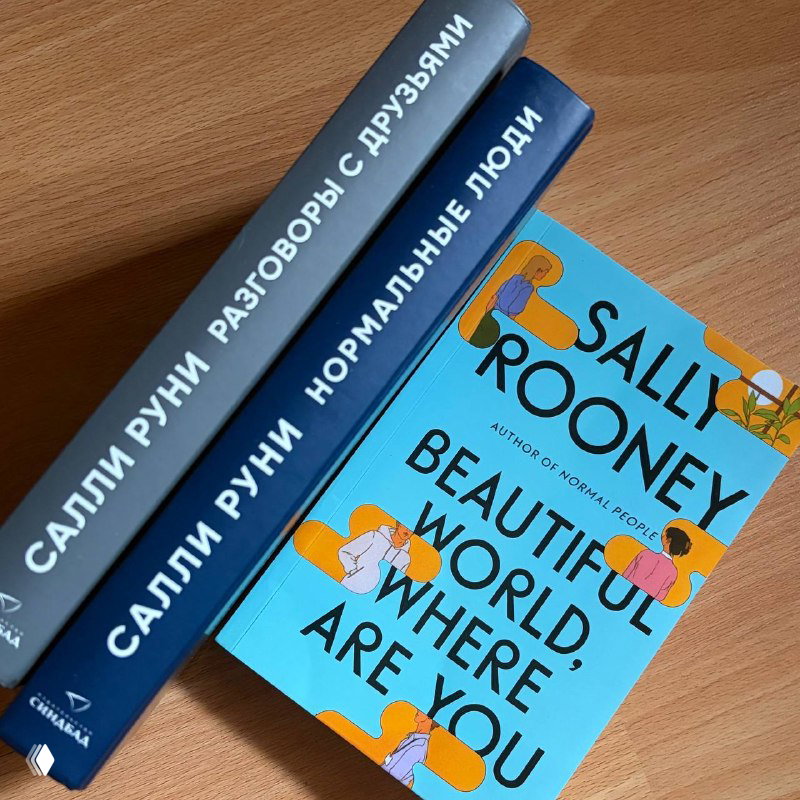 Несколько томов на столе: обложки и корешки русских изданий Салли Руни — сочетание голубой обложки и тёмно-синих переплётов на деревянном фоне.
