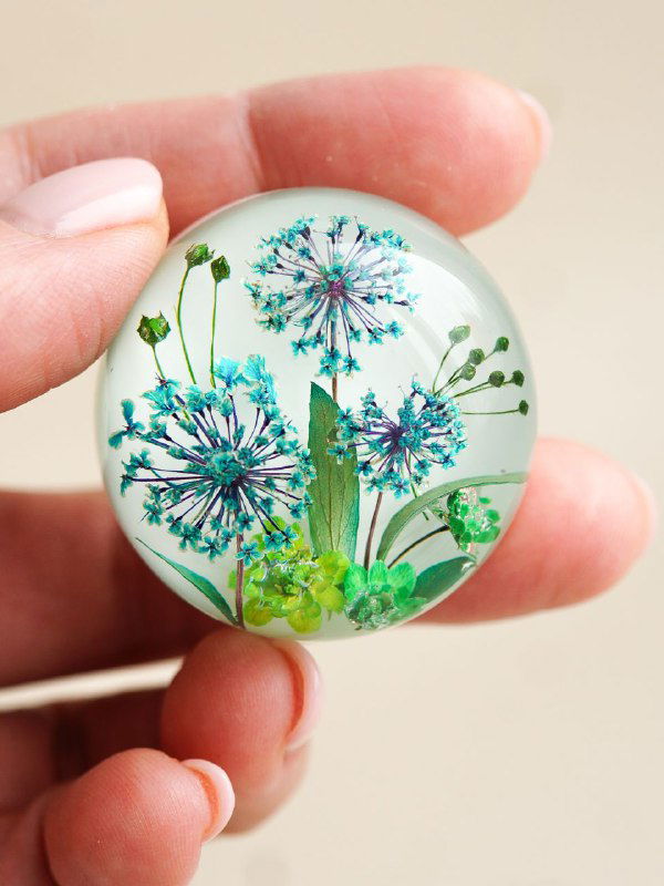 Рукотворная круглая подвеска с засушенными мелкими зонтичными цветами в прозрачной смоле, детализация цвета и фактуры.