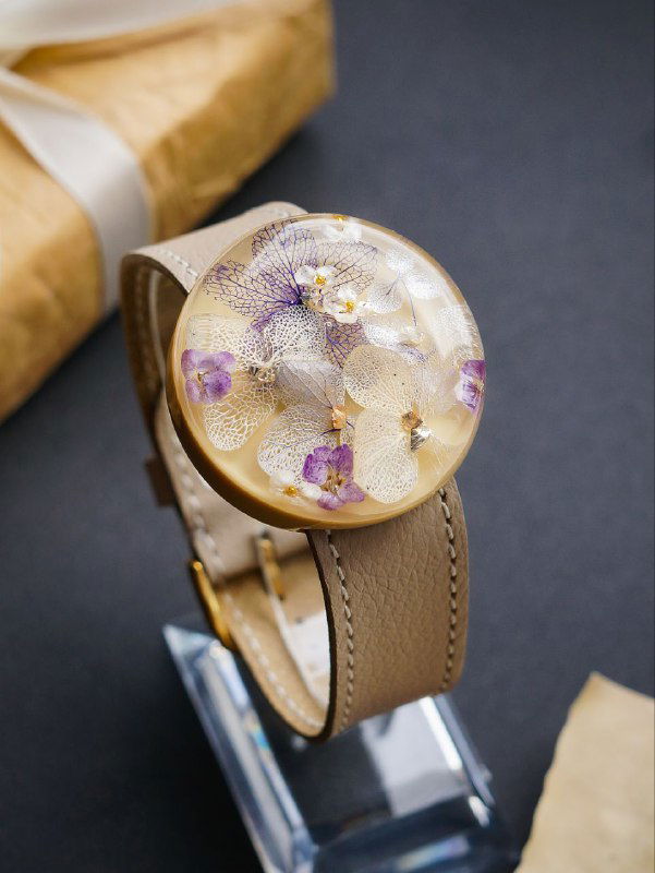 Круглый браслет‑медальон из прозрачной смолы с расположенными внутри сухими цветами, нейтральный фон и показана фактура изделия