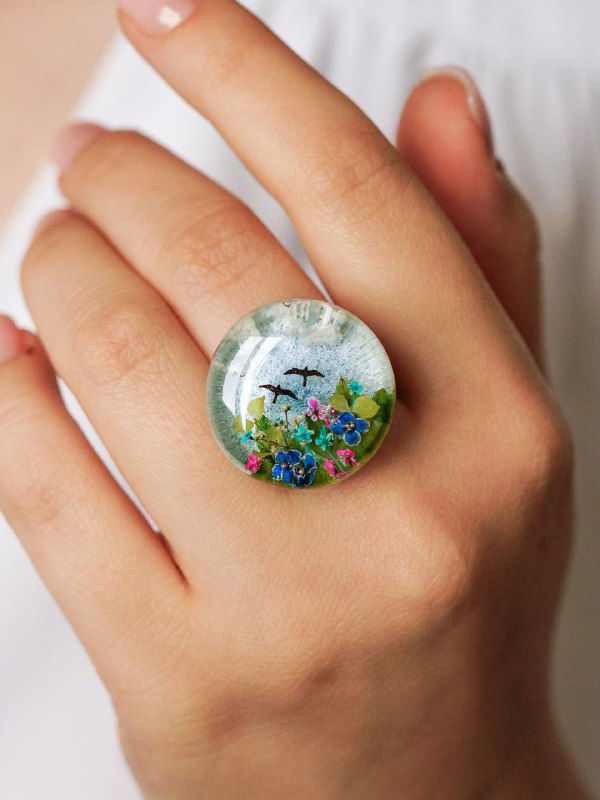 Кольцо с выпуклым прозрачным кабошоном из смолы, внутри миниатюрный пейзаж и крошечные цветы алиссума на пальце модели