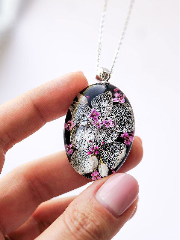 Овальный подвес из чёрной смолы с белыми и розовыми цветами, тонкие детали листьев и фактура сеттингов видны в крупном плане