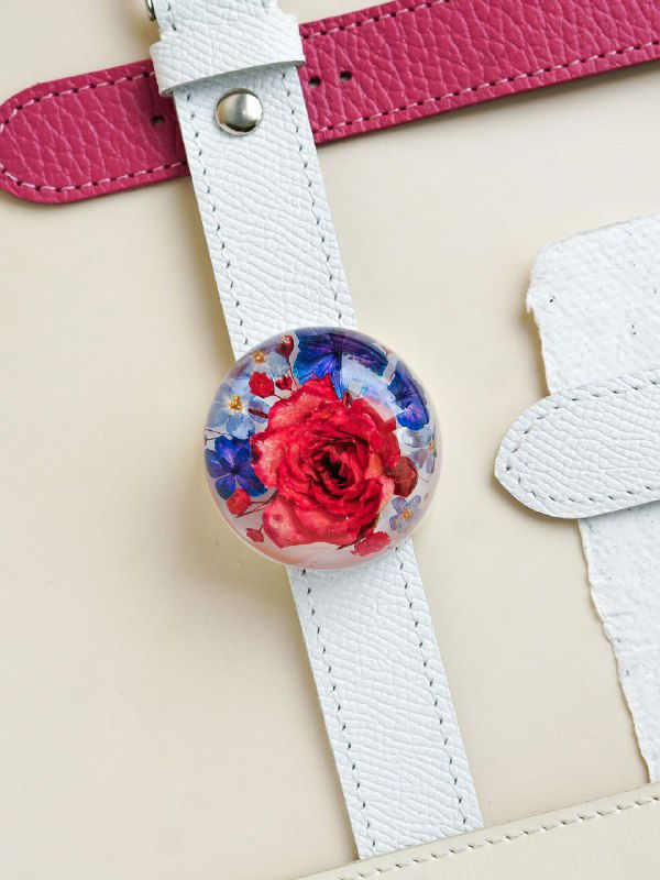Небольшой смоляной кулон с яркой красной розой в центре на светлом фоне; украшение закреплено на белом кожаном ремешке для браслета.