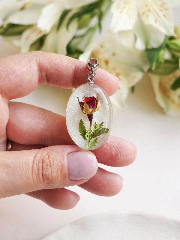 Овальный прозрачный кулон со застывшим внутри бутоном розы и зелёными листиками на светлом фоне, подвеска на металлическом колечке.