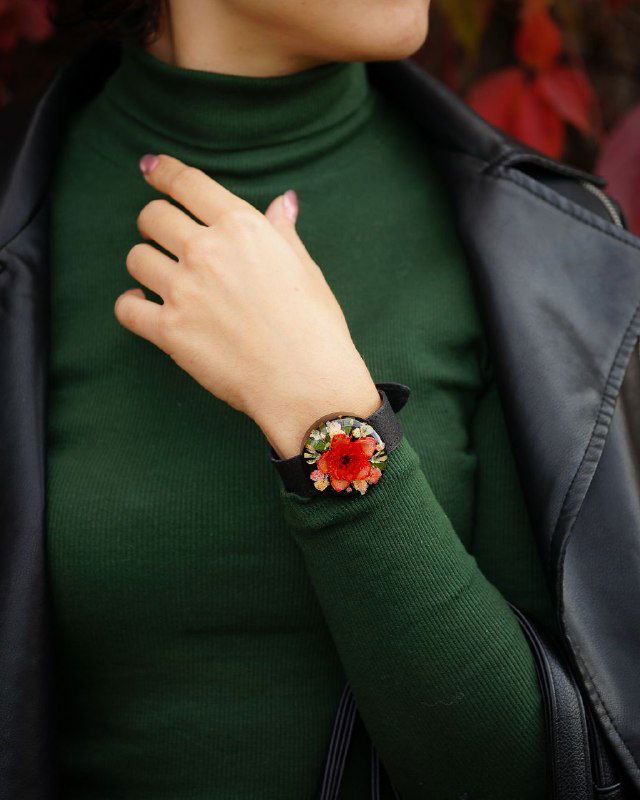 Женский образ: запястье в зелёном свитере украшено браслетом с большим смоляным элементом, внутри которого красный цветок и зелень.