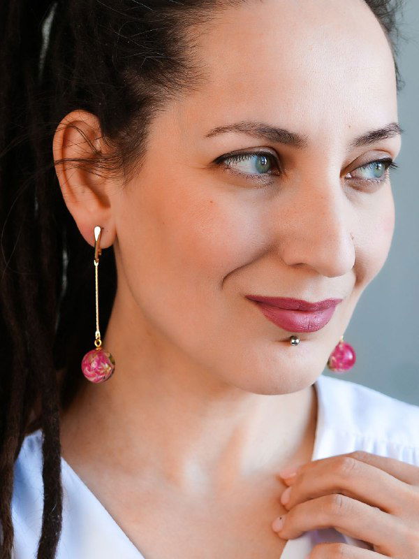 Портретная фотография: женщина в серьгах из прозрачной смолы с маленькими розовыми бутончиками, серьги висят и мягко отражают свет.