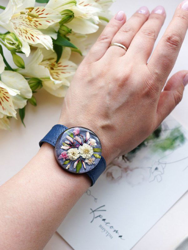 Наручные часы с круглым циферблатом из смолы и вставленными цветами жемчужницы, фотография на руке для масштаба и демонстрации ношения.