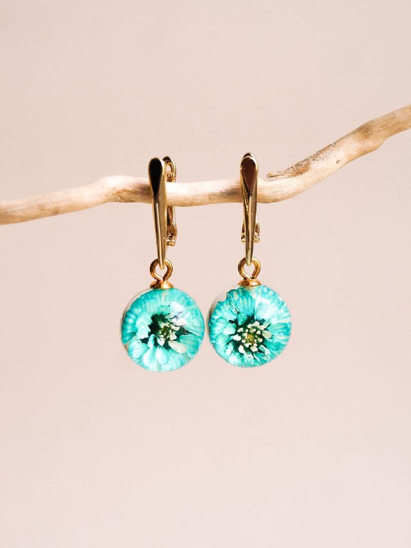 Пара серьг‑капель в бирюзовой гамме с вкраплениями мелких цветков жемчужницы, висящие на тонкой опоре, демонстрация цвета и прозрачности смолы.