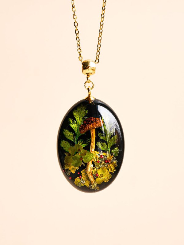 Овальный медальон на цепочке с композицией из папоротника и сухих трав, фон нейтральный, акцент на деталях и текстуре зелёных листьев.