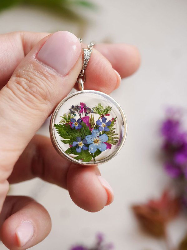 Кулон-жетон с миниатюрным букетиком из синих и фиолетовых цветков и зелёных листочков — авторская работа в руке мастера, макросъёмка.