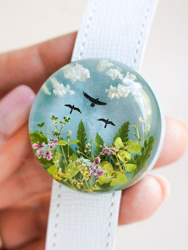 Круглый брелок с изображением мини-поля: зелень, мелкие цветки и силуэты летающих птиц — декоративный мотив с природными элементами.
