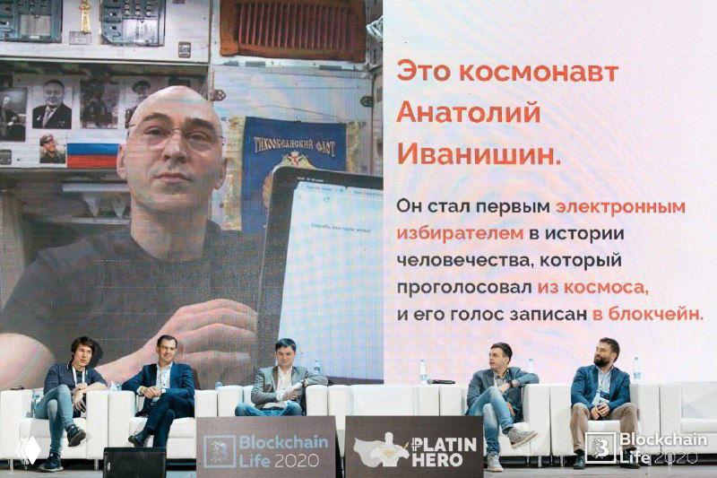 Слайд с портретом космонавта и пояснением о голосовании из космоса; внизу сцена и панель спикеров обсуждают блокчейн-кейс live.