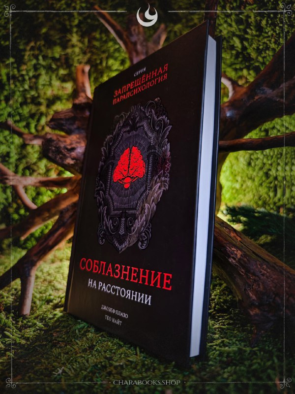 Книга «Соблазнение на расстоянии» под углом: тёмная обложка с красным символом и орнаментом, размещена на мху, вид в перспективе.