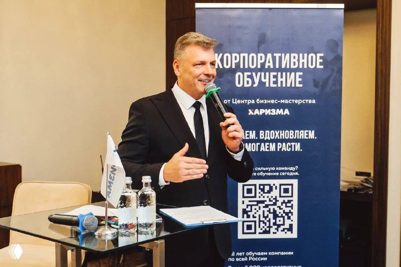 Спикер выступает у трибуны с микрофоном; за ним баннер с надписью про корпоративное обучение и логотип центра Харизма.