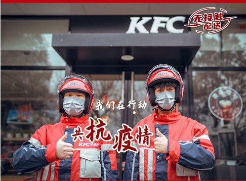 Два курьера KFC в масках позируют у входа в ресторан с жестом одобрения; кадр рекламирует коллективную ответственность и безопасность.