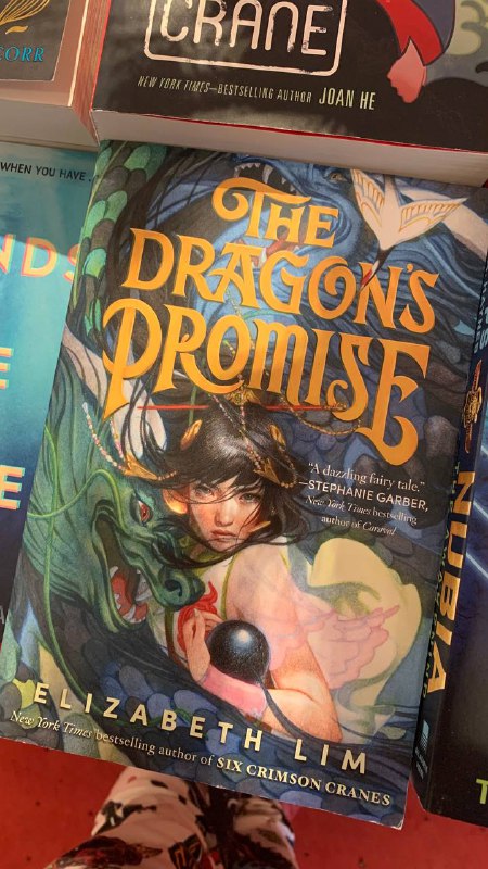 Обложка 'The Dragon's Promise' на полке: фэнтезийный арт с драконом и молодым героем, зеленовато-золотая палитра и крупный английский заголовок.
