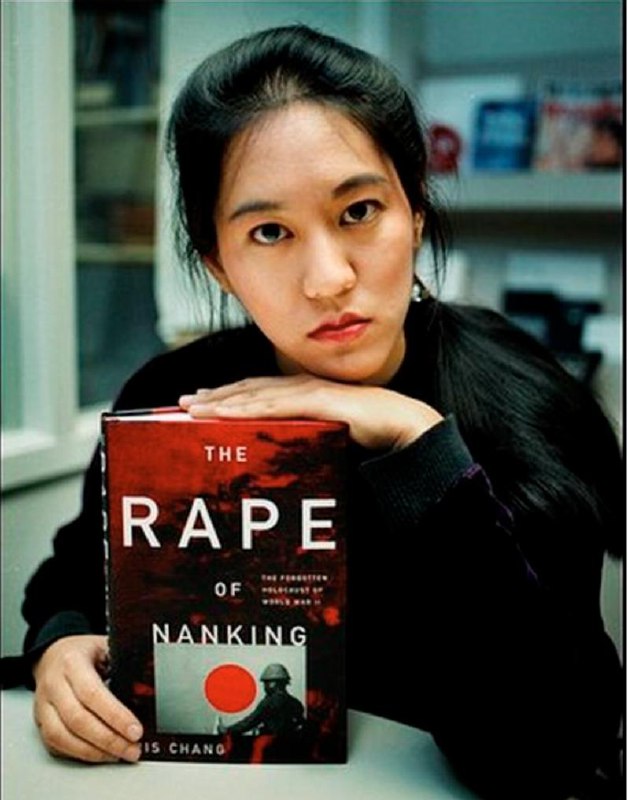 Айрис Чан держит английское издание The Rape of Nanking: портретная фотография женщины с книгой на переднем плане и книжными полками на заднем