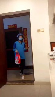 Кадр вертикального видео: человек в синей защитной одежде и маске стоит в дверях квартиры с бытовым фоном — бытовая сцена, вероятно из Китая.