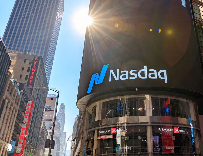 Городская площадь с крупным табло Nasdaq — символ фондового рынка, влияющего на стоимость компаний и важность корпоративного бренда в финансовой среде.