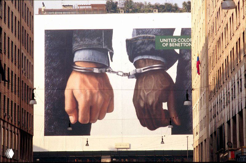 Большой уличный билборд Benetton с изображением запястий в наручниках — контрастные руки и тема заключения, визуальная провокация в городском пространстве.