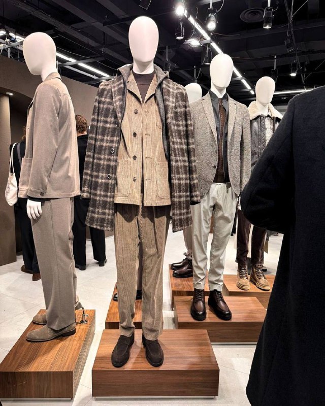 Группа манекенов с образами DIGEL Move: клетчатые и однотонные комплекты на деревянных подиумах, выставочная атмосфера Pitti Uomo с фокусом на текстуры и сочетания.