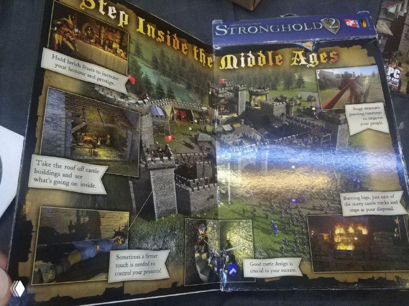 Разворот коробки Stronghold 2: полноцветный разворот/плакат с кадрами игры, иллюстрациями замков и текстовыми блоками на блестящей поверхности.