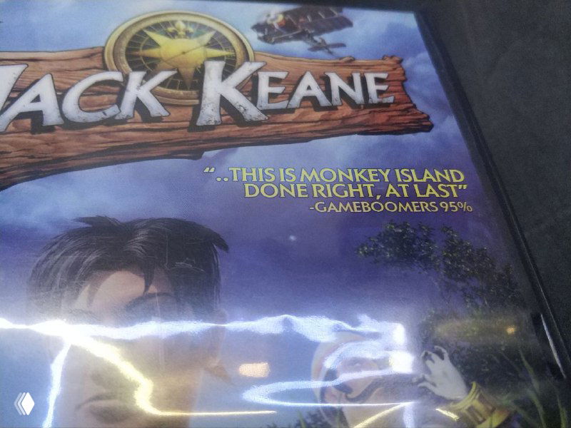Крупный план лицевой части коробки Jack Keane с видимой цитатой о Monkey Island и отражением света на защитной плёнке.