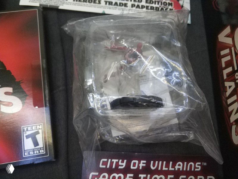 Миниатюра Heroclix в запаянном пластиковом пакетике на фоне вкладыша с надписью City of Villains — близкий план фигурки из комплекта.