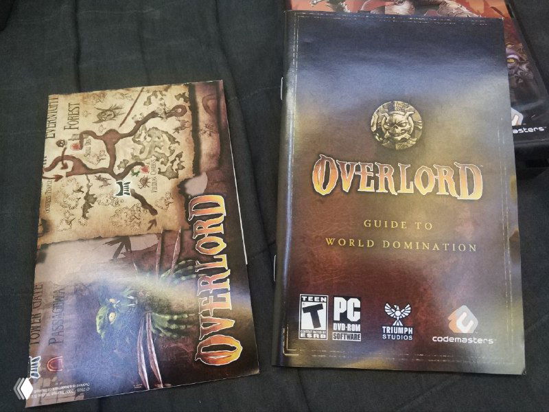 Разложенные внутри обложки и буклеты Overlord: титульный лист «Guide to World Domination» и сопутствующие вкладыши рядом друг с другом.