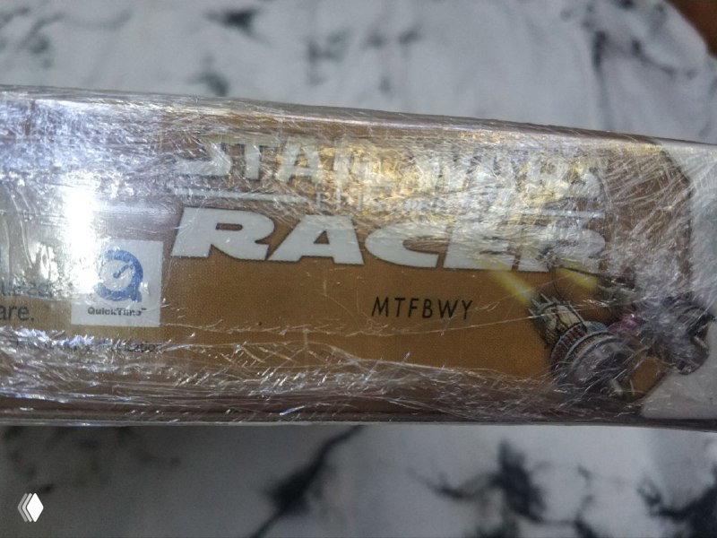 Крупный план боковой кромки коробки Star Wars Racer в плёнке, видна тиснёная надпись «RACER», следы заводской упаковки и часть серийного кода для инвентарного учёта коллекции.
