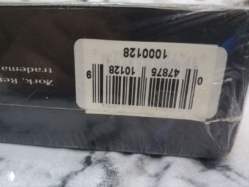 Крупный план переклеенного штрихкода на упаковке Return to Zork: видна наклейка, штрихкод и складки пленки на углу коробки