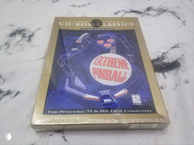 Фото лицевой стороны запечатанного издания Extreme Pinball в золотистой коробке серии CD-ROM Classics на мраморном столе.