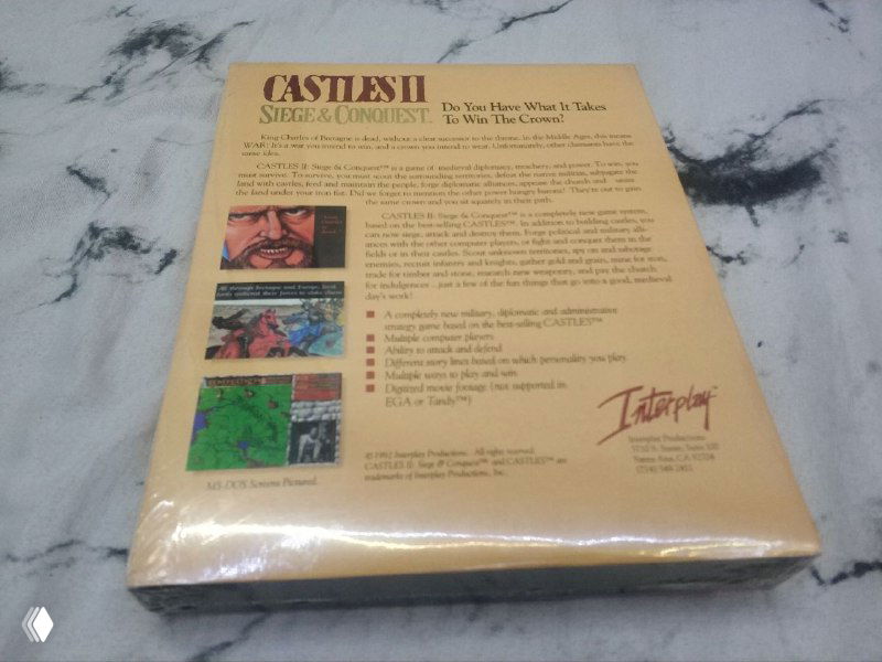 Задняя сторона коробки Castles II: виден текст описания, скриншоты и логотип Interplay на фоне мрамора, коробка в запакованном виде.