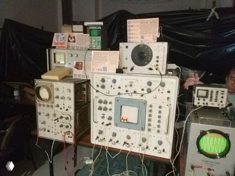 Крупный план ряда осциллографов с круглыми и квадратными экранами, панели управления и провода; на переднем плане видны контрольные таблички и элементы ретро‑оборудования.