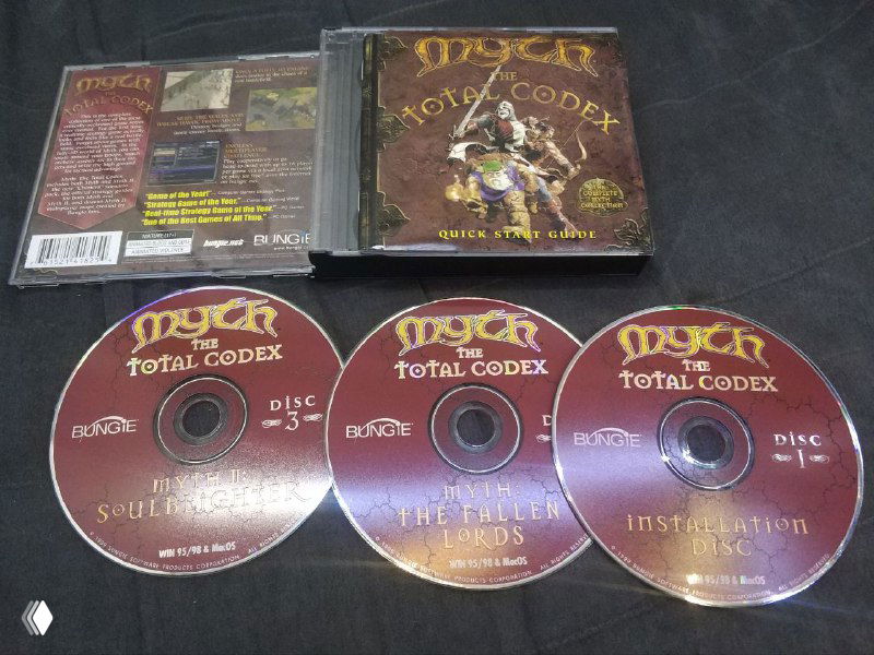 Три компакт-диска из сборника Myth: The Total Codex выстроены в ряд рядом с джевелом; видно маркировку дисков и печать названия на поверхности.