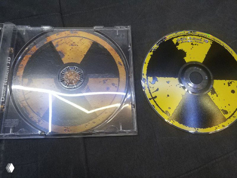 Два диска с жёлто-чёрным радиоактивным принтом и отражениями света рядом с прозрачным джевелом — общий вид коллекционных дисков лота.