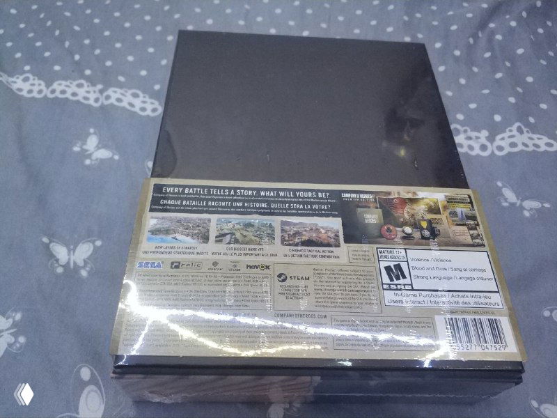 Задняя сторона коробки Company of Heroes 3 Premium Edition с информацией о содержимом и маркировкой, упаковка запечатана и отражает свет от лампы.