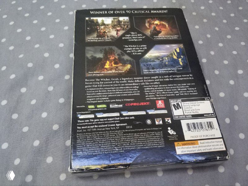Задняя сторона запечатанной коробки The Witcher: Enhanced Edition (2007) с текстом описания, скриншотами и штрихкодами, снимается на том же фоне.