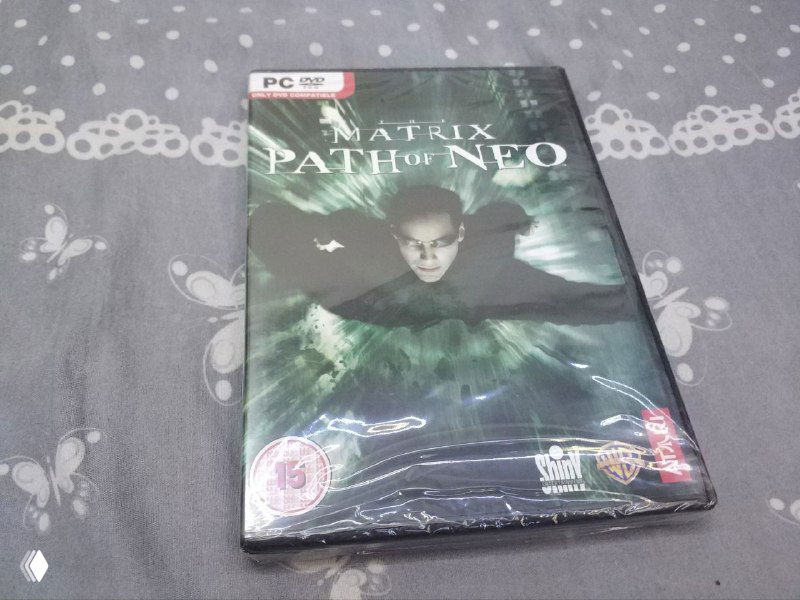 Запечатанная передняя обложка Matrix: Path of Neo (британское издание) для PC — виден логотип игры, возрастной ценз и пластиковая плёнка поверх коробки.