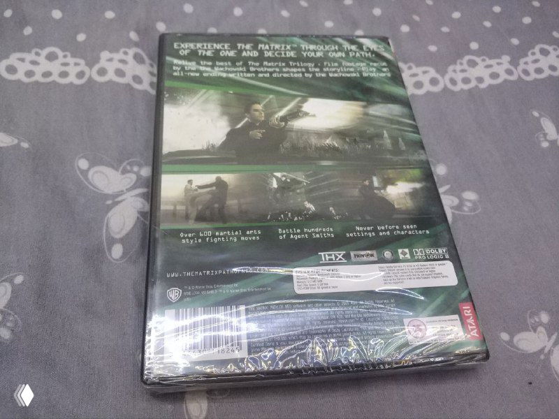 Задняя сторона коробки Matrix: Path of Neo с информацией об издании, системными требованиями и скриншотами, всё запечатано и лежит на том же фоне.