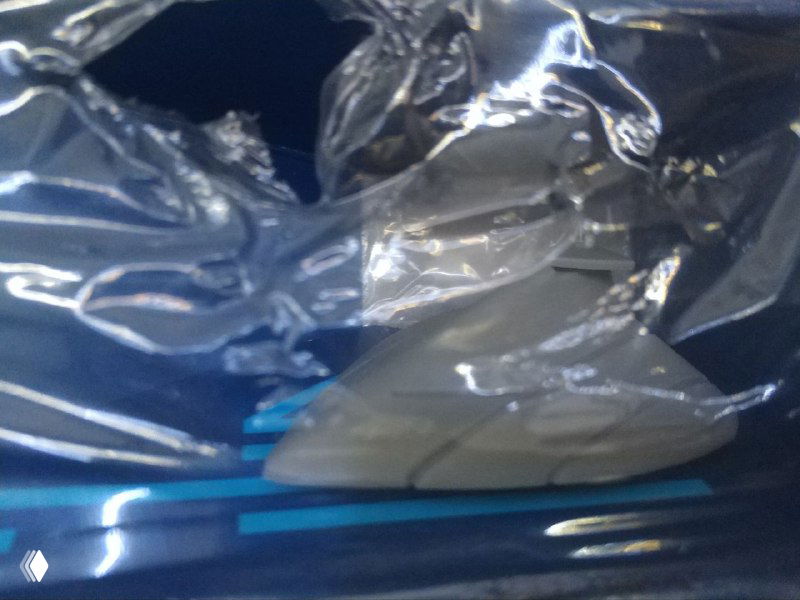 Крупный план места в верхней части коробки: рваная плёнка и небольшая фигурка под ней, заметна часть пластика и попытка извлечь фигурку.