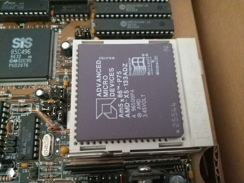 Крупный план процессора AMD X5-133ADZ на плате, окружённый микросхемами памяти и маркировкой на кристалле и плате.