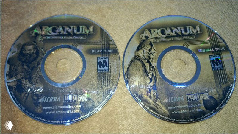 Два установочных диска Arcanum (Sierra) на фоне: видны издательские надписи, пометки Play Disc и Install Disc, металлический отблеск поверхности.