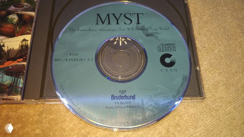 Крупный план компакт-диска Myst (1994) в прозрачном контейнере с печатью издателя и маркировкой, отличающейся по цвету и плотности накатки.