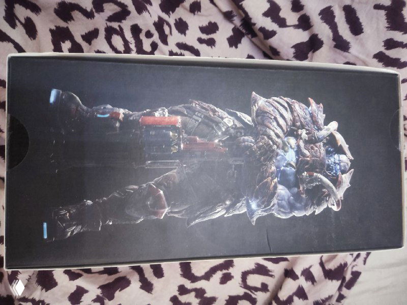 Боковая сторона коробки с фигурой Scalebearer — изображение персонажа на тёмном фоне, фото ориентации портрет, коробка лежит на ткани.