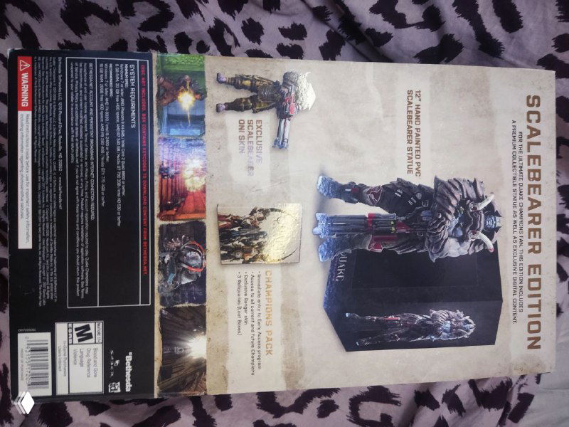 Задняя сторона коробки Quake Champions Scalebearer Edition с описанием содержимого издания и иллюстрациями — видно текст и изображения аксессуаров внутри издания.