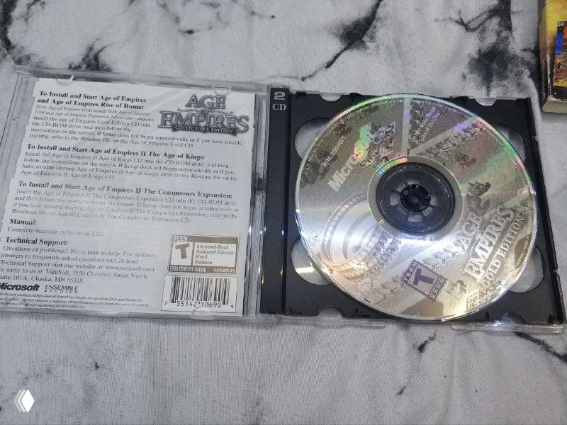 Открытый тонкий джевел Age of Empires: вид на внутреннюю сторону обложки с текстом и один из компакт-дисков в лотке, видны наклейки и инвентарные надписи.
