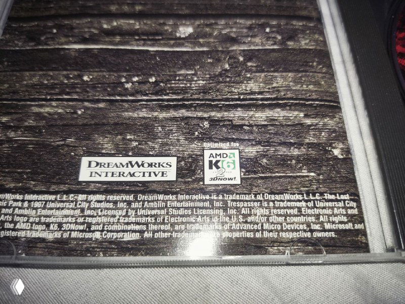 Крупный план задней части вкладыша джевела Trespasser: логотип DreamWorks Interactive, значок совместимости AMD K6/3DNow! и мелкий печатный текст.